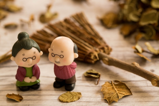 落ち葉とほうきを背景にした老夫婦のミニチュア人形
